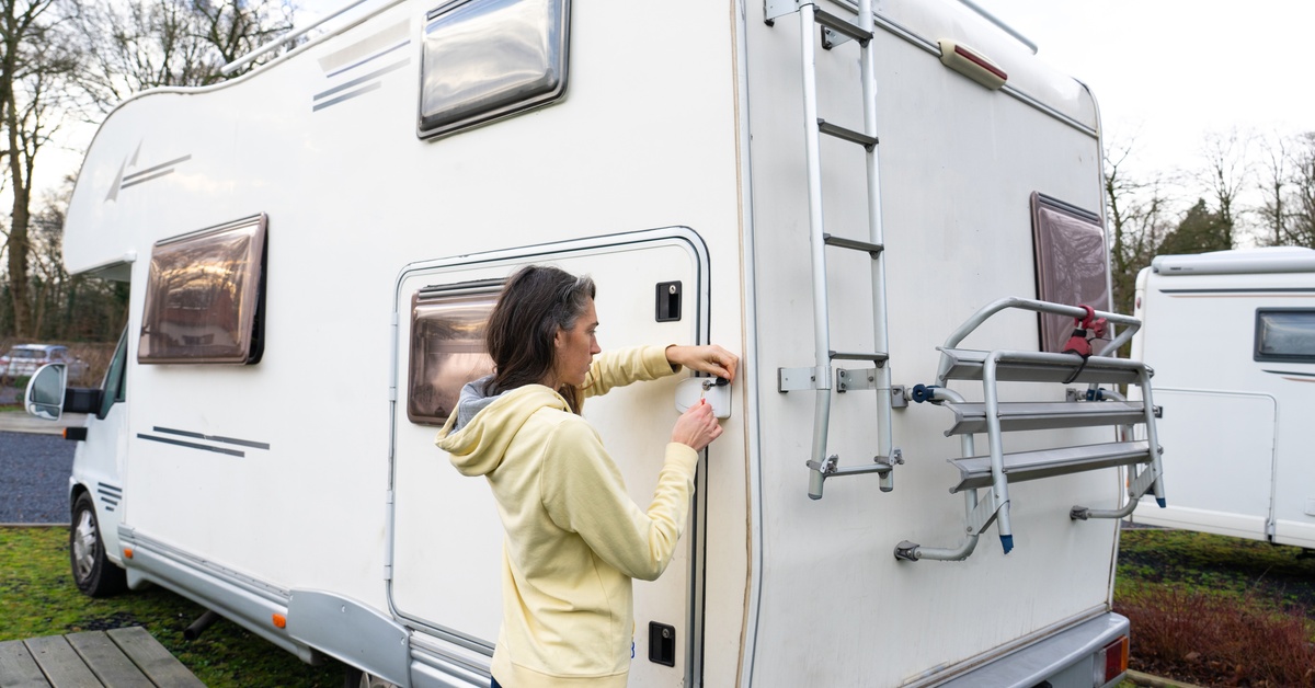 A woman in a yellow hooded sweatshirt using a key to open an exterior compartment on the side of a white RV.