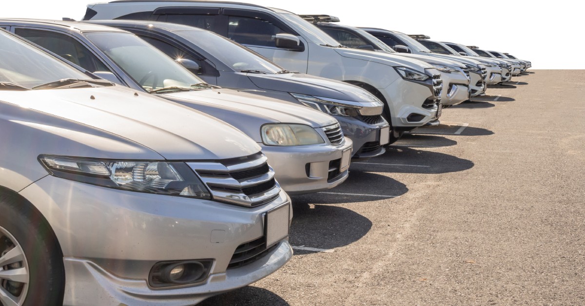 A row of silver and white SUVs and sedans parked next to each other in a parking lot on a sunny day.